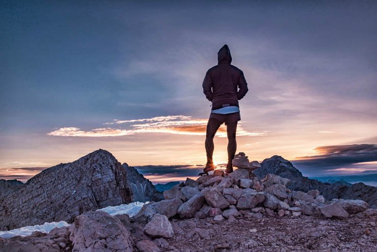 man standing rocks sweatshirt sunset
