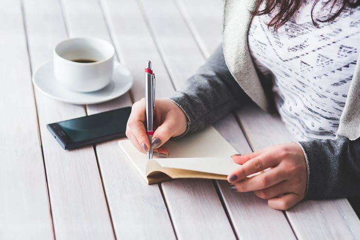 write writing mobile tech technology woman female cup mug desk pen notebook coffee
