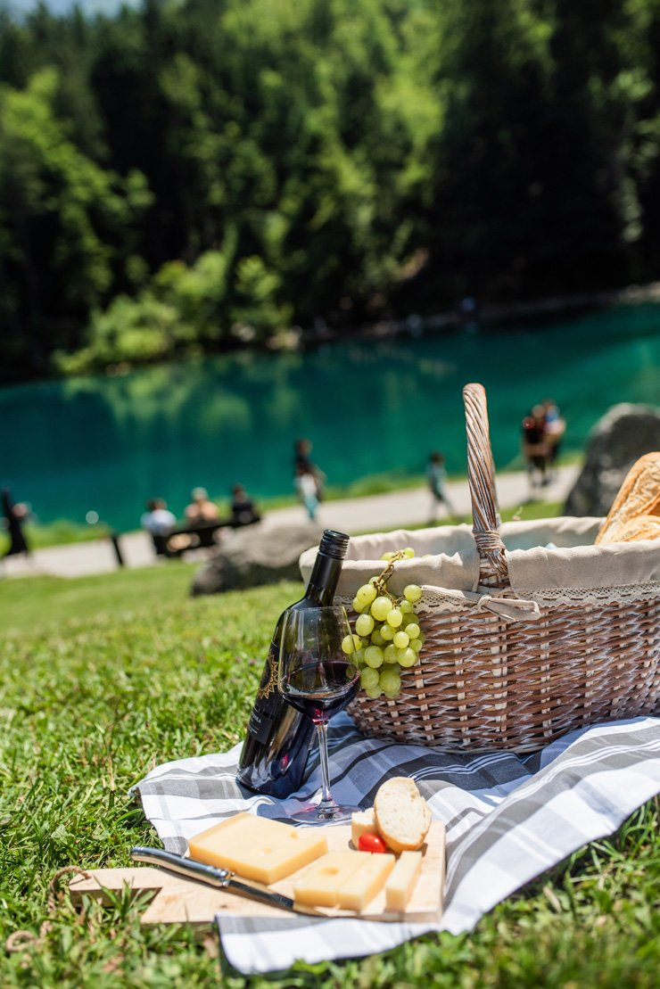 picnic outdoor lifestyle food summer wine bread cheese mat rug grass lake grapes grape basket bucket
